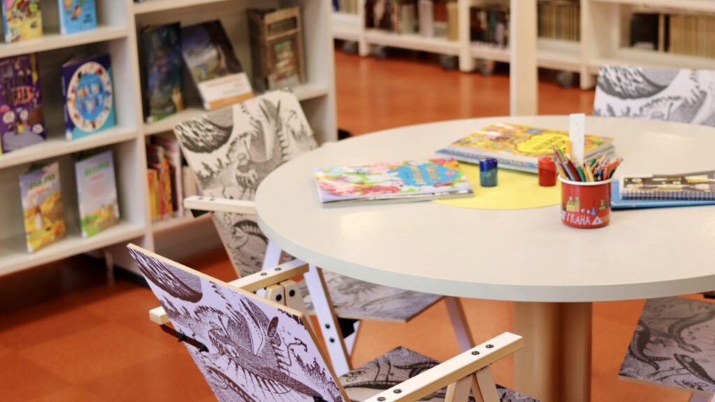 Muumi-aiheisia tuoleja Multian kirjaston lastenosastolla. Pöydällä kyniä ja puuhavihkoja.