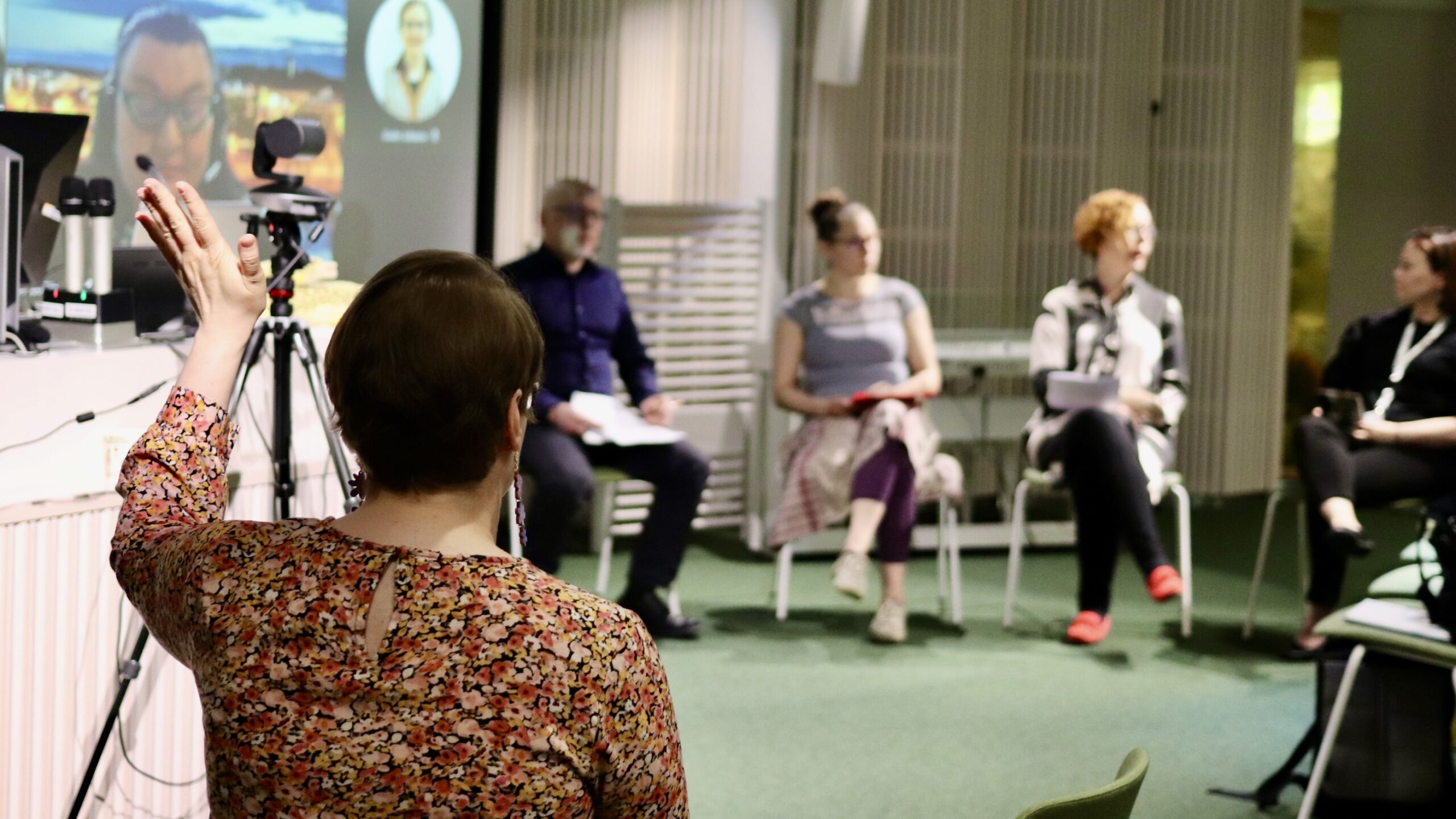 Yksi ihminen selkä kameraan päin. Taustalla neljä ihmistä keskustelee.