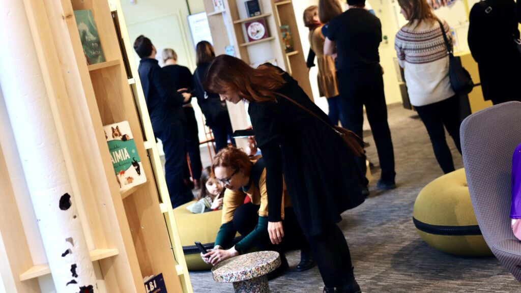 Ihmisiä kumartuneena kuvaamaan kirjastosalissa.