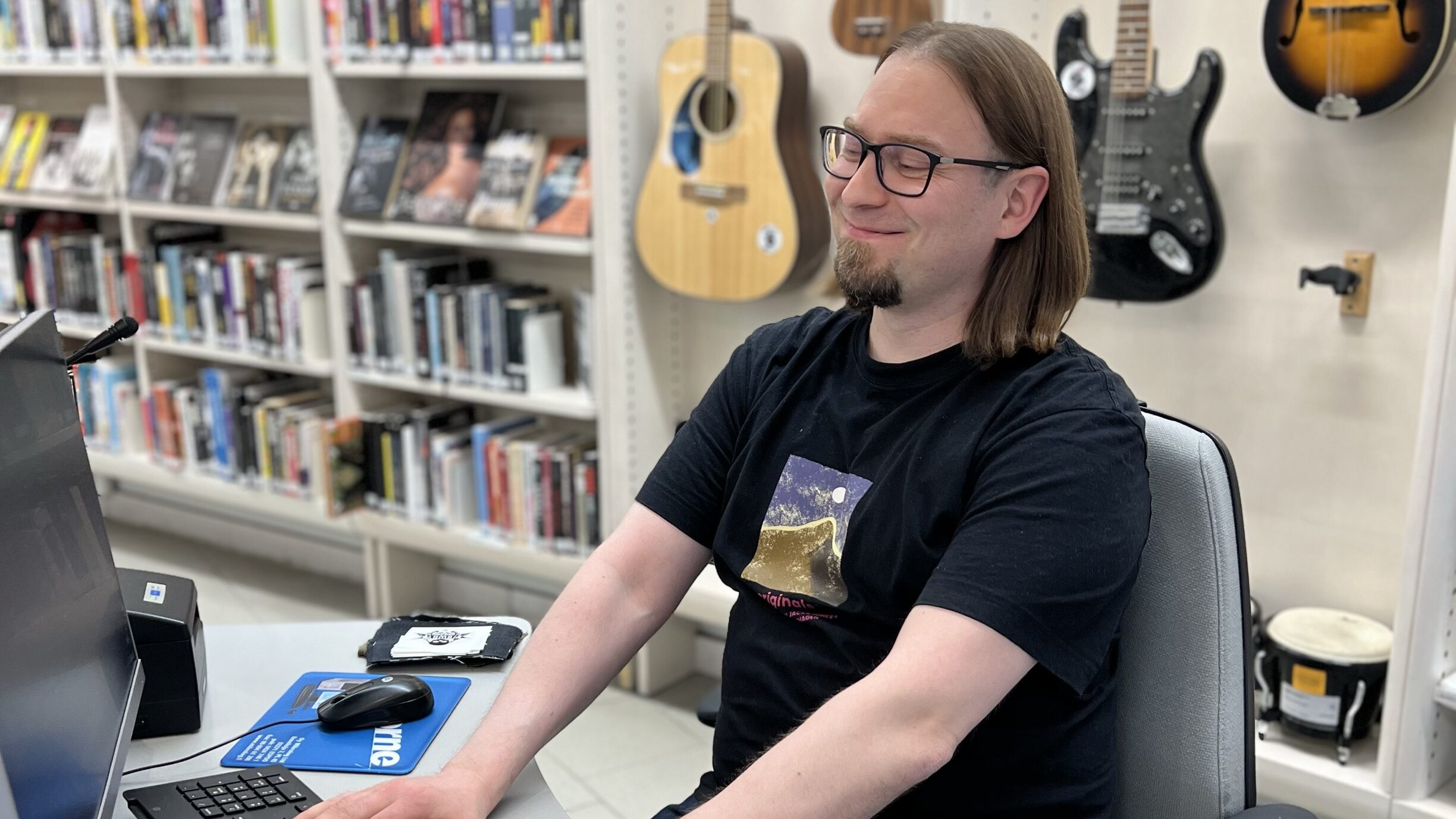 Ihminen istuu tietokoneen äärellä kirjastossa