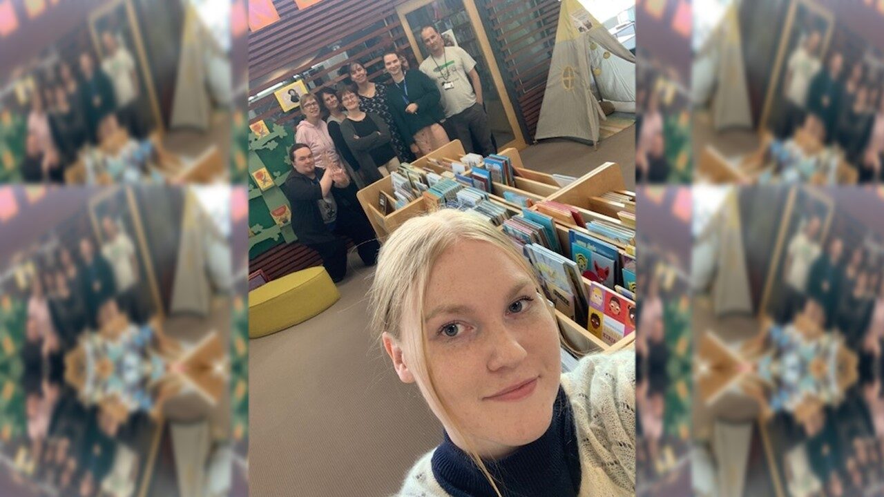 Yksi ihminen edessä ja seitsemän ihmistä taustalla kirjaston lastenosastolla.