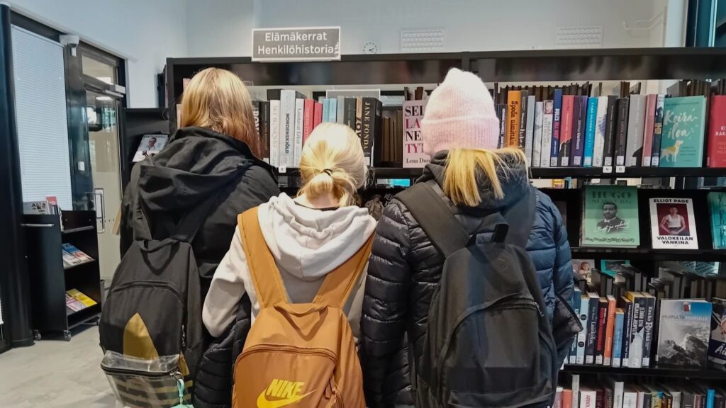 Kolme nuorta kirjastossa, selät kameraan.