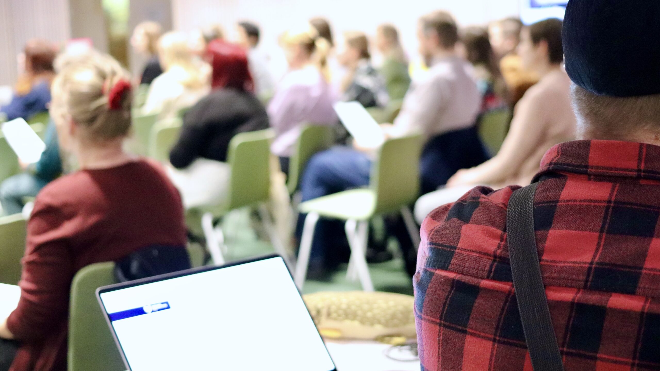 Ihmisiä luentosalissa. Etualalla kannettava tietokone.