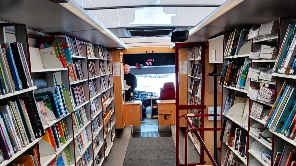 Keuruun kirjastoauton hyllyjä ja taustalla kirjastoauton kuljettaja
