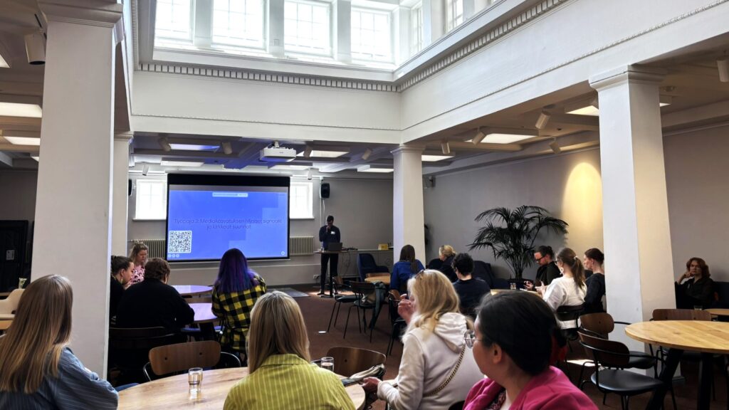 Työpajaan osallistuvia ihmisiä istuu pöydissä