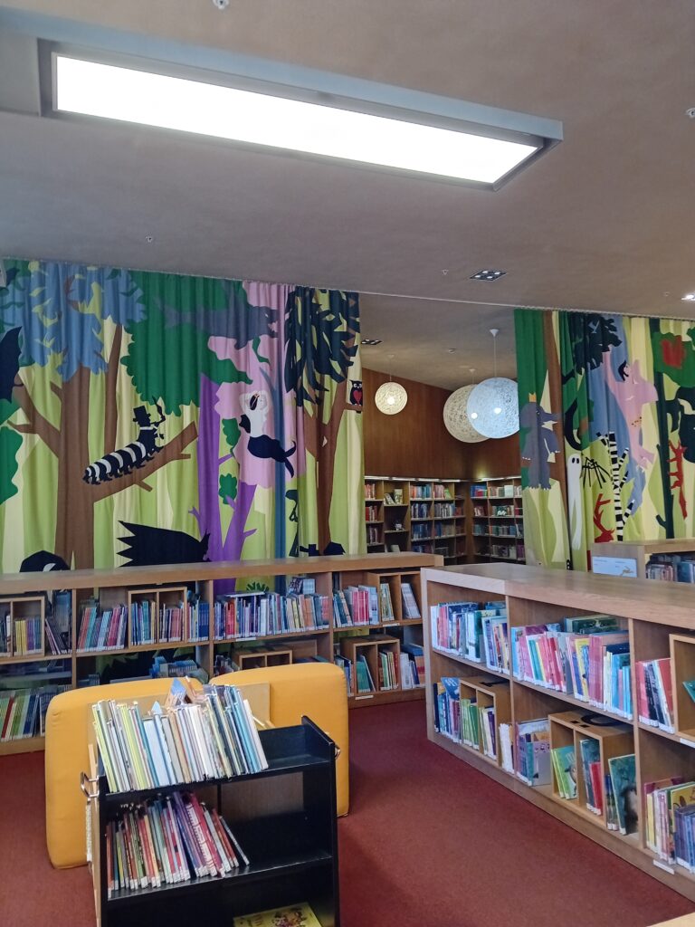 Turun pääkirjaston nuortenosasto. Etualalla matalia kirjahyllyjä, taustalla tilan rajaava värikäs verho.