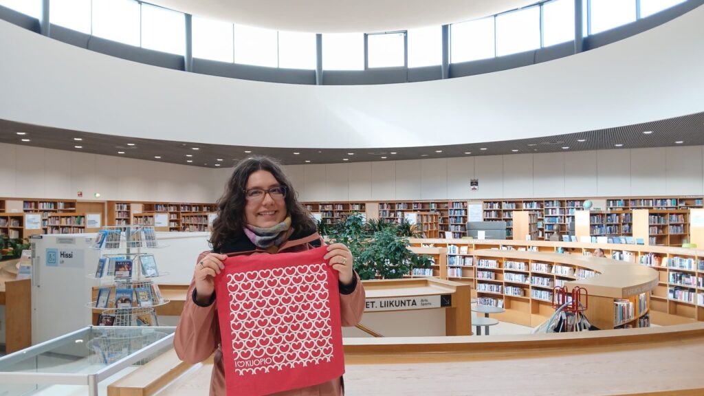 Erika hymyilee Kuopion pääkirjastossa käsissään "I love Kuopio" -kangaskassi.