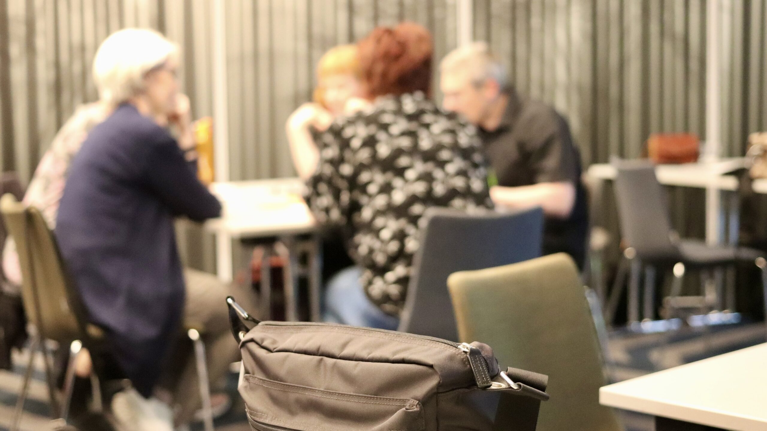 Etualalla käsilaukku. Takana ihmisiä pöydän ääressä istumassa.