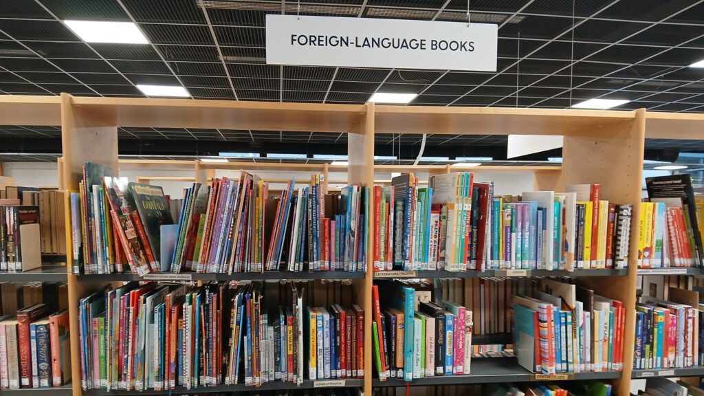 Puijonlaakson lähikirjaston monikielinen kirjahylly, jonka yläpuolella kyltti "Foreign-language books".
