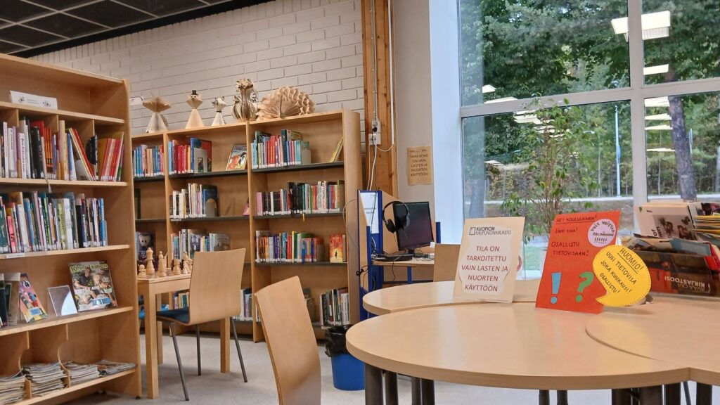 Puijonlaakson lähikirjaston lastenosaston kirjahyllyjä ja pöytäryhmiä. Pöydällä kyltti "Tila on tarkoitettu vain lasten ja nuorten käyttöön".