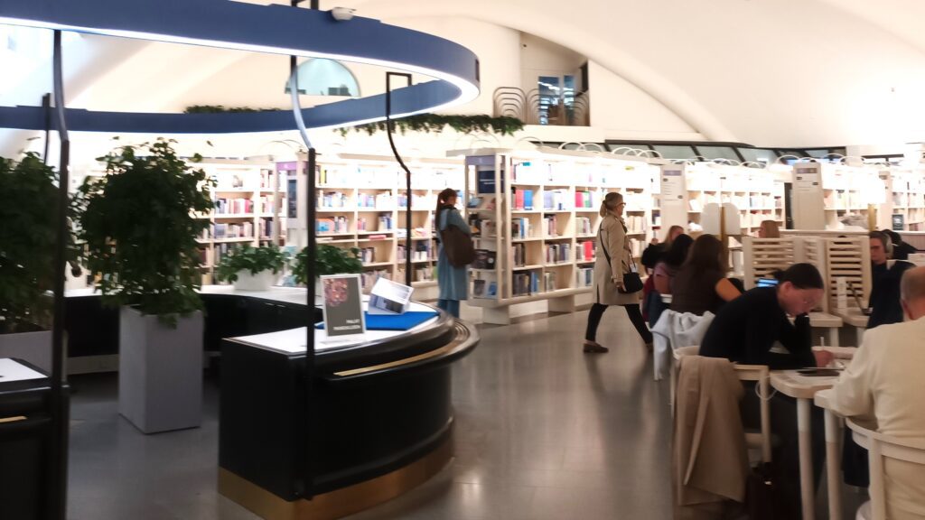 Ihmisiä istumassa ja liikkumassa kirjastosalissa.