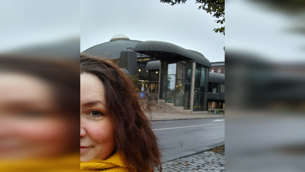 Taustalla pääkirjasto Metso, etualalla ihminen katsoo kameraan. Puolet kasvoista näkyy.