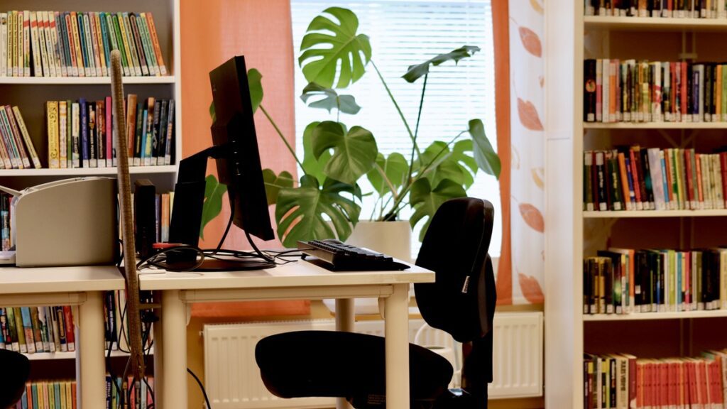 Kirjaston asiakaspäätteellä varustettu työpiste Luhangan pääkirjastossa. Taustalla huonekasvi ja kirjahyllyjä.