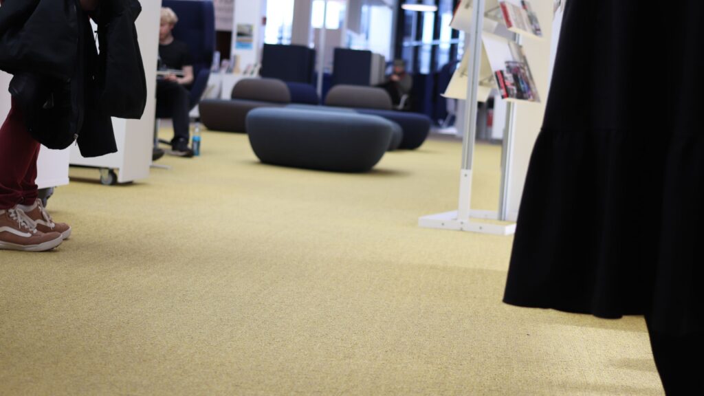 Keltainen kokolattiamatto peittää Virran ylimmän kerroksen kirjastosalin lattiaa.