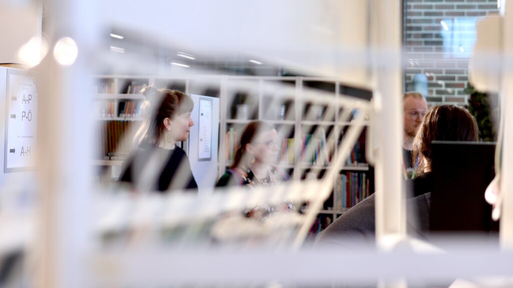 Etualalla metallinen kirjaesittelyteline, taustalla näkyy ihmisiä.