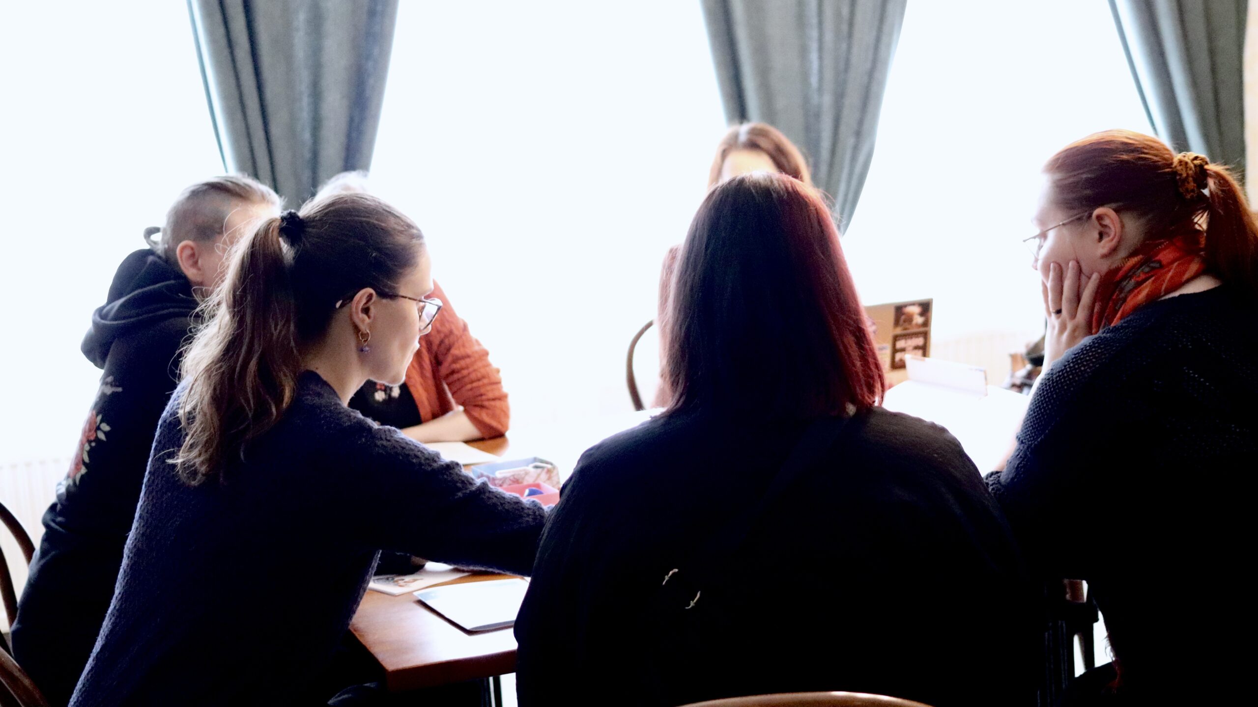 Ihmisiä ringissä pöydän ääressä selin kameraan.