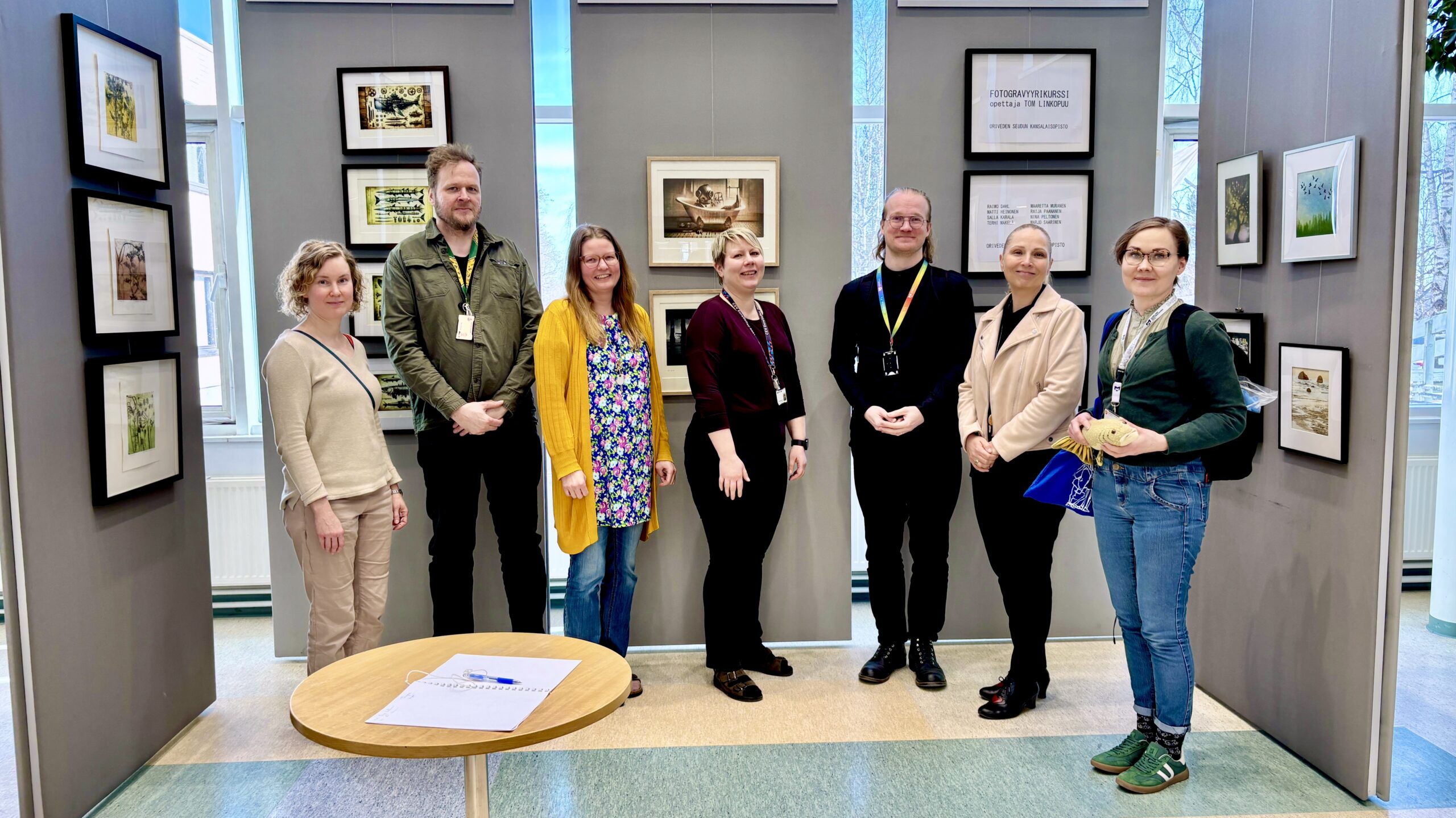 AKE-koordinaattorit ja Oriveden kirjaston henkilökunta poseeraavat kameralle kirjaston näyttelyseinän edessä.