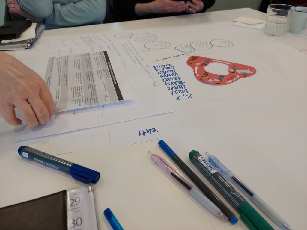 Pöydällä erilaisia kyniä, paperia ja lomakkeita.