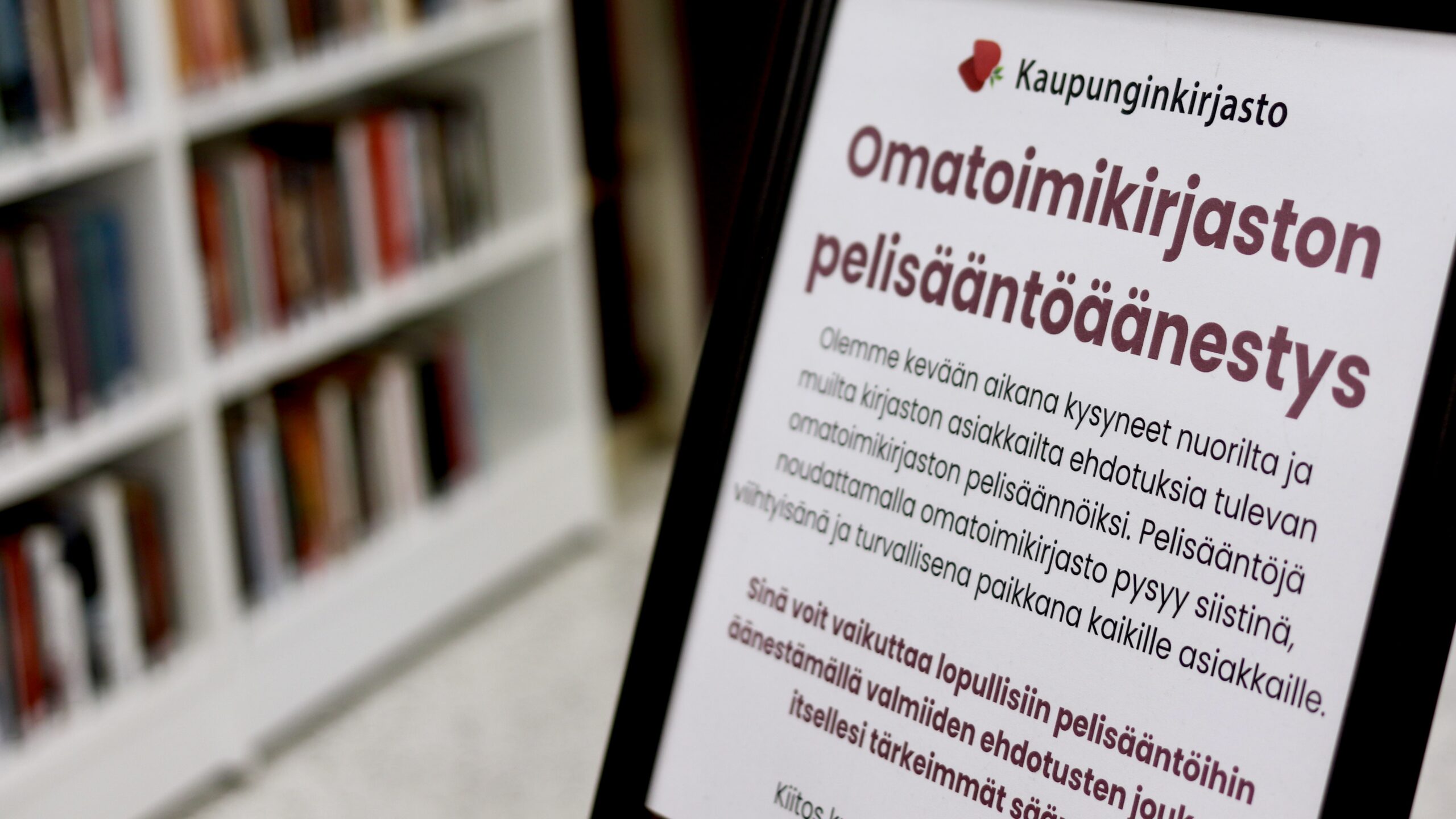 Lähikuva kyltistä, jossa kerrotaan kirjaston asiakkaille suunnatusta omatoimikirjaston pelisääntöäänestyksestä.
